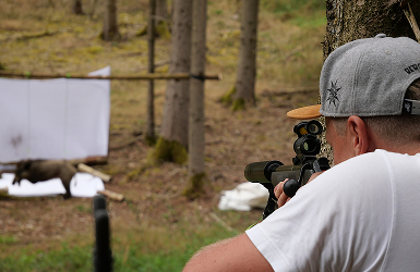 Ein Mann zielt mit einem Gewehr auf ein Ziel hinter einer weißen Leinwand im Wald.